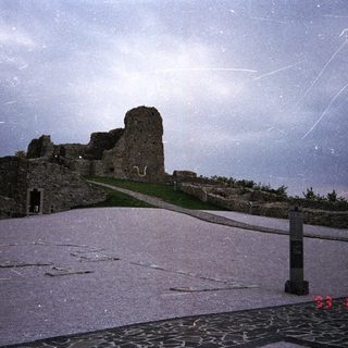 Ruins of a castle overlook a stone path and landscape.