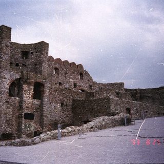 Ruined stone castle with people standing nearby on a platform.