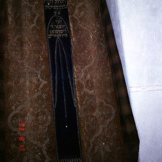Here's a brief summary of the image: A tallit (prayer shawl) hangs on a closet rod.