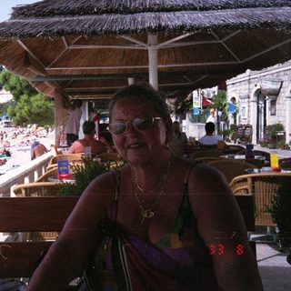 Woman sits under a thatched roof, overlooking a beach.