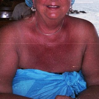 Woman sits near the water, wearing a blue headscarf.