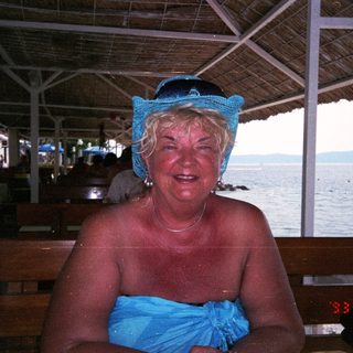 Woman sits near the water, wearing a blue headscarf.