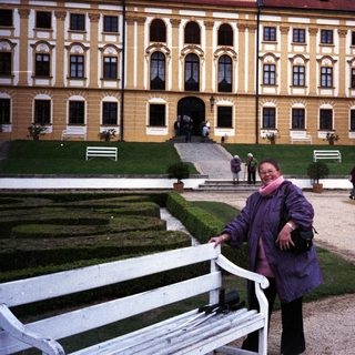 Woman poses in front of an ornate, yellow palace.