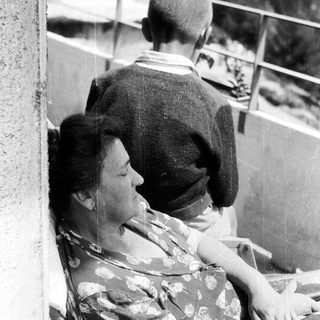 Here's a brief summary of the image: Woman resting on a chair, man standing nearby.