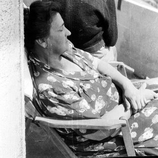 Here's a brief summary of the image: Woman resting on a chair, man standing nearby.