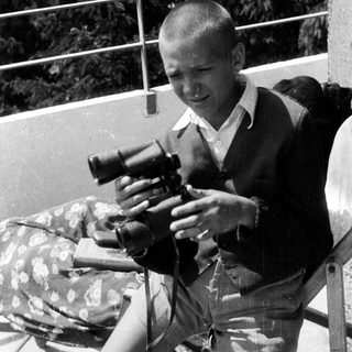 Here's a brief summary of the image: Young boy holding a camera outdoors, likely taking a picture.
