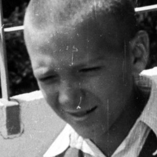 Here's a brief summary of the image: Young boy holding a camera outdoors, likely taking a picture.