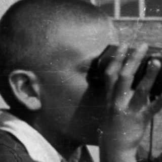 Boy uses binoculars while standing on a balcony.