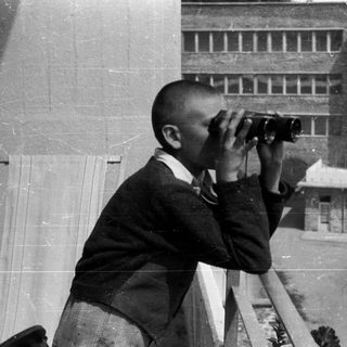 Boy uses binoculars while standing on a balcony.