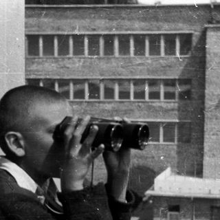 Boy uses binoculars while standing on a balcony.