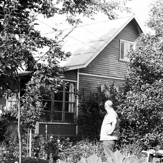 Man stands near house, surrounded by trees and foliage.