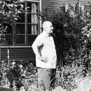 Man stands near a house in a wooded, overgrown area.