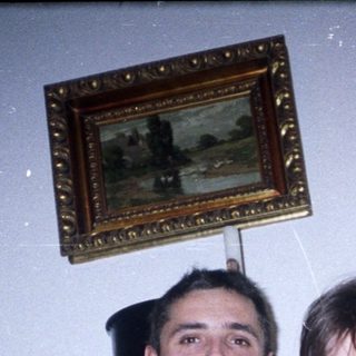 Two people pose indoors near a dark wood cabinet.