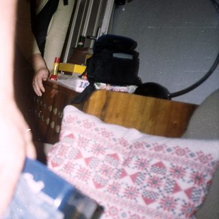 Arm holding a watch, near a bed and furniture.