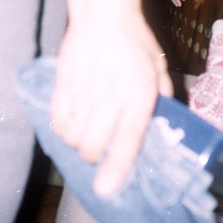 Arm holding a watch, near a bed and furniture.
