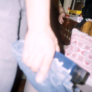 Arm holding a watch, near a bed and furniture.