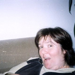 Here's a brief summary of the image: Person with dark hair smiling on a textured couch.