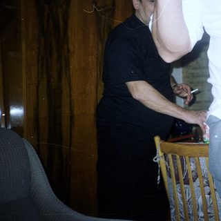 Man in white shirt stands near person smoking indoors.
