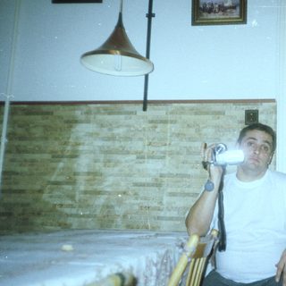 Man sits with camera, seemingly in a kitchen setting.