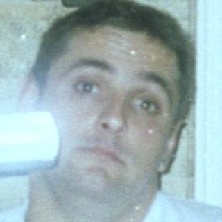 Man sits with camera, seemingly in a kitchen setting.