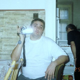 Man sits with camera, seemingly in a kitchen setting.