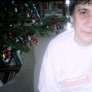 Here's a brief summary of the image: Woman sits with wine and dessert near a Christmas tree.