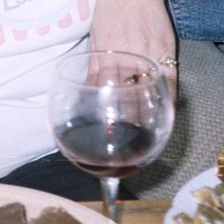 Here's a brief summary of the image: Woman sits with wine and dessert near a Christmas tree.