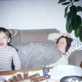 Boy makes silly face; woman relaxes on a sofa.
