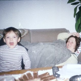 Boy makes silly face; woman relaxes on a sofa.