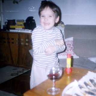Girl stands near table with wine glass and food.