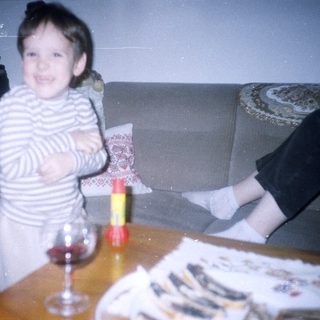 Girl stands near table with wine glass and food.