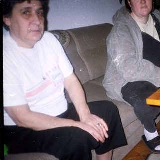 Two people seated on a couch, drinks and food nearby.