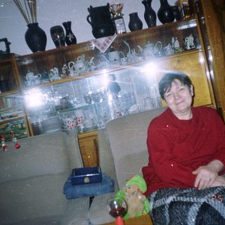 Woman sits in a chair with a decorated shelf behind.