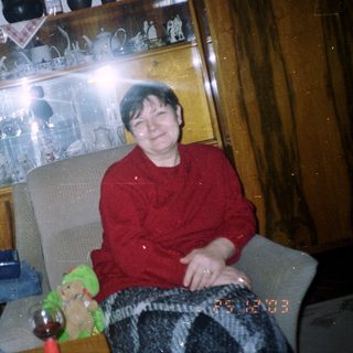 Woman sits in a chair with a decorated shelf behind.