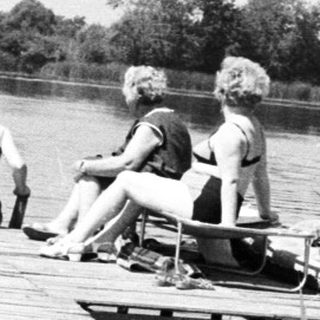 People sit on a wooden dock over a body of water.