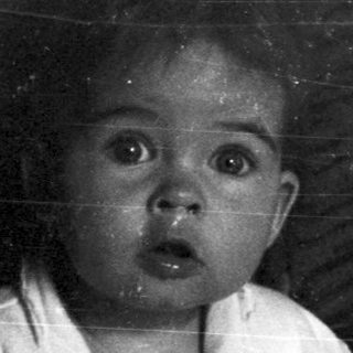 Here's a brief summary of the image: Baby sitting on a pot, looking directly at the camera.