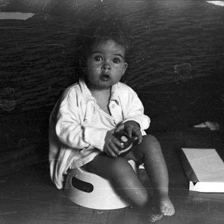 Here's a brief summary of the image: Baby sitting on a pot, looking directly at the camera.