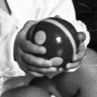 Baby sits on potty, holding a ball, looking distressed.