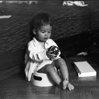 Here's a brief summary of the image: Baby sitting on a potty, holding a toy.