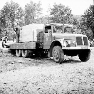 Truck transporting a large load with workers nearby.