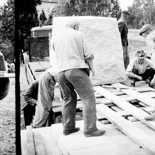 Men moving a large stone slab onto a wooden pallet.