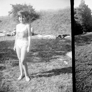 Girl in bikini standing on grassy hill, others nearby.