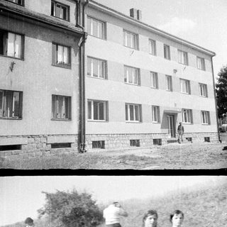 Here's a brief summary of the image: People relaxing near a building, two girls in swimsuits.