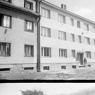 Here's a brief summary of the image: People relaxing near a building, two girls in swimsuits.