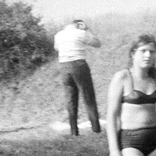Here's a brief summary of the image: People relaxing near a building, two girls in swimsuits.