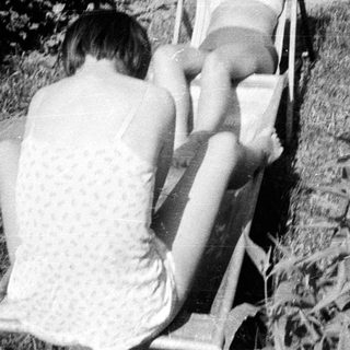 Here's a brief summary of the image: Young person reclining on a chair in a grassy area.