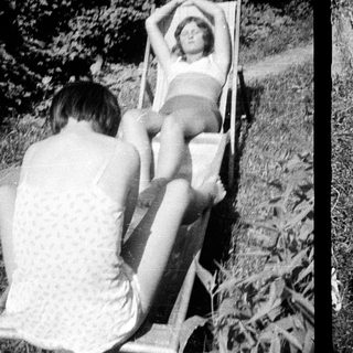 Here's a brief summary of the image: Young person reclining on a chair in a grassy area.