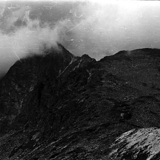 Dramatic, cloudy mountain peak with textured, weathered rock formations.