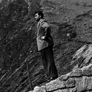 Man stands near a stone wall overlooking a mountain range.