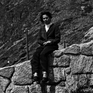Woman sits on a wall with a mountain in background.